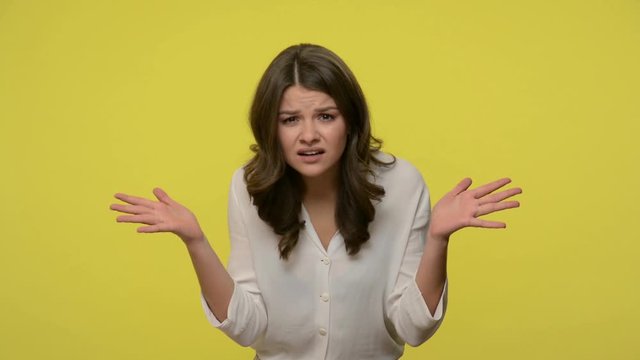 What, how could you? Confused woman with brunette hair in blouse standing with raised hands, asking what's reason why, indignant annoyed expression. indoor studio shot isolated on yellow background