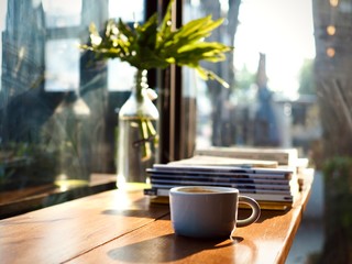 Hot coffee in a white ceramic cup is served on a wooden counter next to the glass wall in the morning.With interesting books.