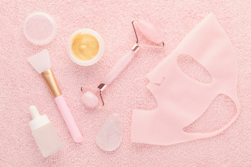 golden facial cream mask with a brush, jade roller, face serum and silicone beauty mask on pink...