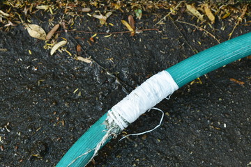 crack green watering rubber tube repairing by white tape roll with dry leaf on frontyard garden ground