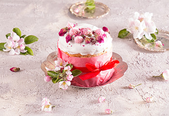 Happy Easter decoration for greeting card. Easter cake with white icing, marshmallows, dry rose and fresh blooming apple flowers and rose color craft paper on gray background..