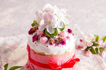 Happy Easter decoration for greeting card. Easter cake with white icing, marshmallows, dry rose and fresh blooming apple flowers and rose color craft paper on gray background..