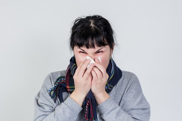 isolated portrait of young caucasian or asian brunette woman with red sore eyes blowing her runny...