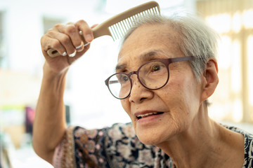 Closeup of face of beautiful old people brushing hair with comb in her hand,happy asian senior woman enjoy combing hair,clean healthy woman's hair,female elderly care her hair, beauty concept