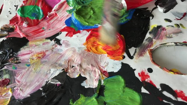Close up of artist brush mixing yellow and red colors. Colorful image from an artist’s studio or a school showing creative education. 