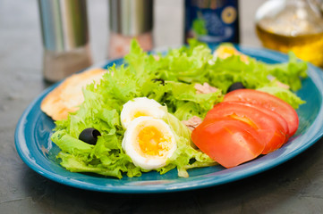 Salad with tuna, eggs, tomato, olives, spices and croutons, sauce or oil on blue plate