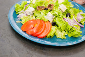 Salad with octopus or squid, cheese, tomato, olives, onions, spices and croutons, sauce or oil on blue plate, copy space.
