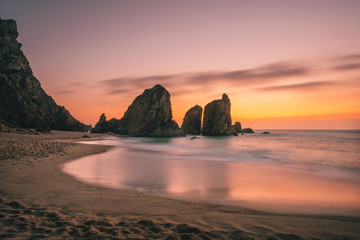 Ursa Beach near Cape Roca at Atlantic Ocean coast in Portugal. Sand beach with sea stacks in evening golden sunset sky