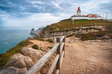 Fototapeta na wymiar Sintra Portugal. Cape Roca and red lighthouse. Cabo da Roca. Travel and tourism landmark with beautiful coastline cliffs of atlantic ocean