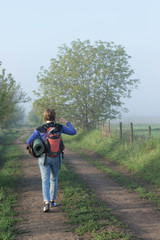 Woman traveler with backpack walking in nature beautiful misty morning in summer space for text back view