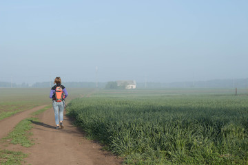 Woman traveler with backpack runs  beautifyl atmospheric misty morning  a house among fields in the background