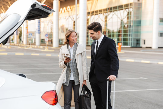 Image of businesslike man and woman standing with luggage by car