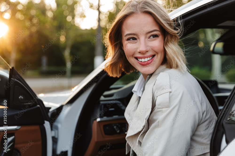 Wall mural Image of young beautiful businesslike woman sitting in luxury car