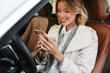 Image of beautiful businesslike woman sitting in car and using cellphone