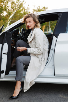 Image of beautiful businesslike woman sitting in car and using cellphone