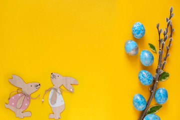Obraz na płótnie Canvas Easter greeting card with blue easter eggs and easter bunny on yellow background. Top view with space for your text.