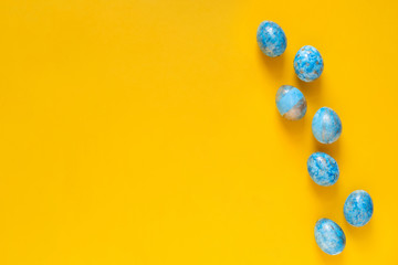 Easter greeting card with blue easter eggs on yellow background. Top view with space for your text.