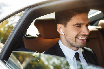 Image of young caucasian businesslike man in suit riding in car