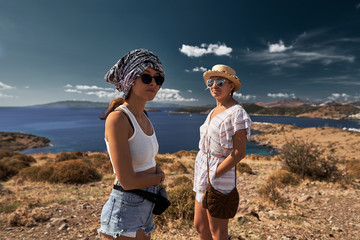 portrait of two young women travelers standing on hill with Bodrum bay on background and looking at camera