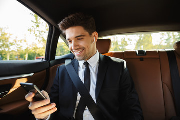 Image of young businesslike man using earbuds and cellphone in car