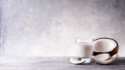 vegetable drink made from coconut in the glass and parts of coconut, on a rustic gray background. Empty space for text