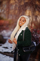 Chic african american blond woman in black leather clothes and green velvet jacket posed in winter sunny day.