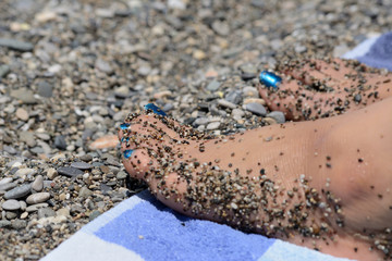 Female feet covered with pebbles on the beach with blue nails