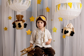 Sweet toddler boy, playing with airplane and teddy bear, air balloons with toys behind him