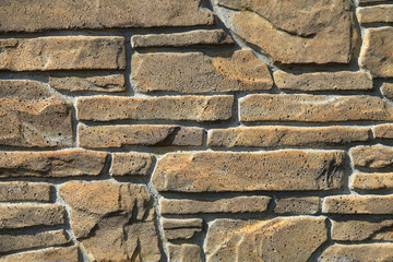 Beige-colored decorative stone wall, texture, background. Tan or light-brown stones of irregular shape in the wall construction. Decorative stone laying. The design of stylish exterior