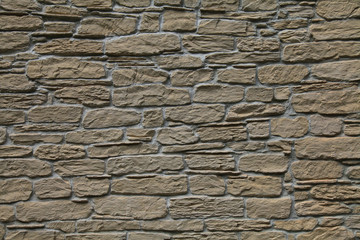 Beige-colored decorative stone wall, texture, background. Tan or light-brown stones of irregular shape in the wall construction. Decorative stone laying. The design of stylish exterior