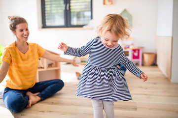 Cheerful young mother with small daughter indoors in bedroom playing.