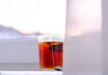 a transparent glass mug of black tea on white windowsill on sky background. Morning. Breakfast.
