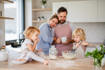 Young family with two small children indoors in kitchen, cooking.