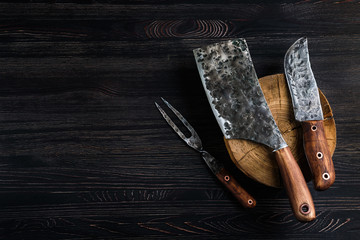 Old butcher meat knife, cleaver and fork on black background - Powered by Adobe
