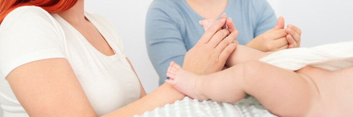 Obraz na płótnie Canvas Female massage therapist teaching young mother how to massage her newborn baby boy. Baby massage concept. Cropped shot close up on hands web banner.