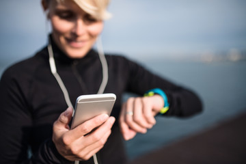 A young sportswoman with smartphone standing outdoors on beach.