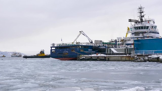 A tug ship sails across the Pacific ocean against the backdrop of snow covered mountains in cloudy weather