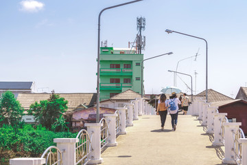 Back view of two women spread an umbrella to block the hot sun during the day to walk across the bridge together to visit the city.