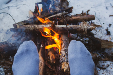 Man's legs against the bonfire in the forest. Bushcraft symbol. Solo survival in nature. Winter in the forest, travel