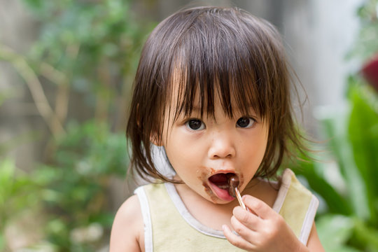 Portrait image of 1-2 yeas old baby. Happy Asian child girl eating a ice-cream brown chocolate by herself. Her face messy and dirty by food.