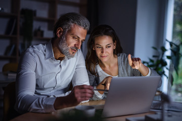 Architects with laptop sitting at the desk indoors in office, working late.