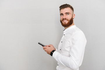 Image of bearded happy man smiling and typing on cellphone