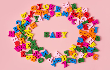 Word baby written in colorful letters in a frame from a bright multi-colored alphabet on a pink background.