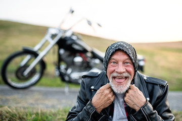 A cheerful senior man traveller with motorbike in countryside, having fun.