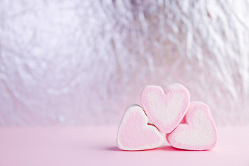 Pastel valentine background made of marshmallows souffle in the form of hearts on a pink and silver background. Valentine's Day concept with copy space