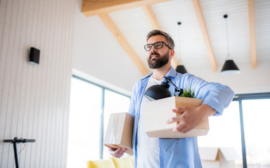 Mature man with boxes moving in new unfurnished house, walking.