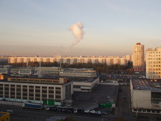 View from a height of the city landscape with office buildings, multi-storey apartment buildings and pipes with smoke on the horizon