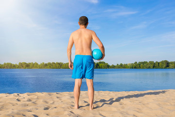 A man with a volleyball ball on the beach on a sunny day. The view from the back.