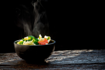 The steam from the vegetables broccoli cauliflower on black bowl , a steaming. Boiled hot Healthy food on table on black background,hot food and healthy meal concept