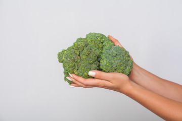 Closeup of female hands holding big green broccoli, fresh raw vegetables, concept of healthy eating and vegetarian diet, low calorie food nutrition. indoor studio shot, grey background, copy space